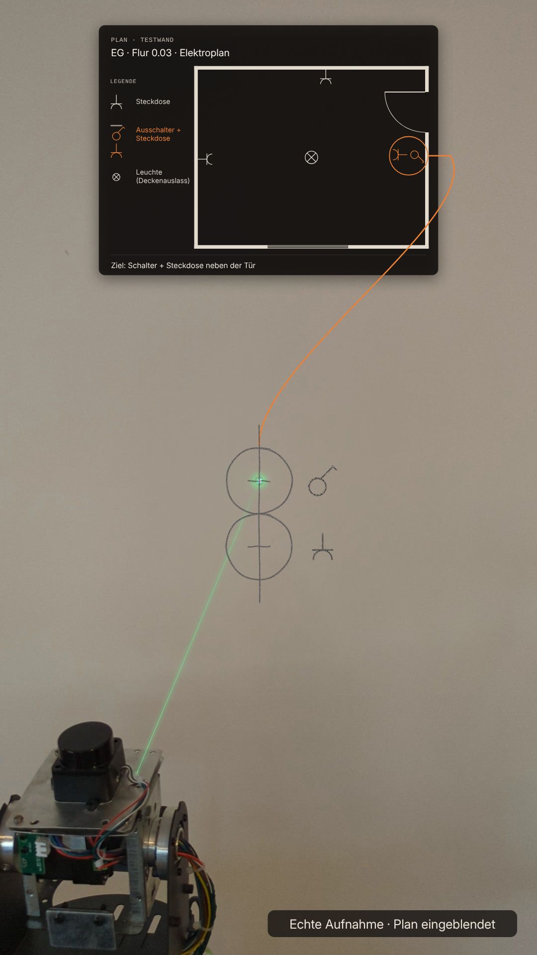 Aufnahme des Aurintex-Beam-Prototyps vor einer blanken Wand. Eingeblendet ist ein Elektroplan. Ein grüner Laserstrahl zeigt die Stelle an der Wand, an der laut Plan Schalter und Steckdose neben der Tür sitzen. Dort erscheinen Bleistiftmarken.